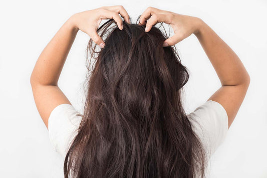 A woman from behind scratching her head and her long, brown, itchy hair extensions.