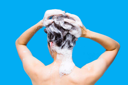 A woman from behind washing her thinning hair on a blue background.