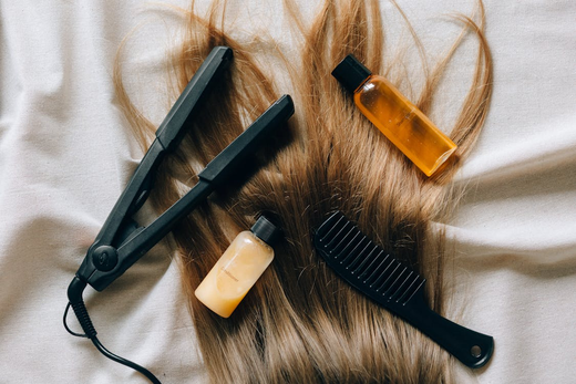 A selection of hair products for wigs, including a styling iron and comb, laid on a sheet.