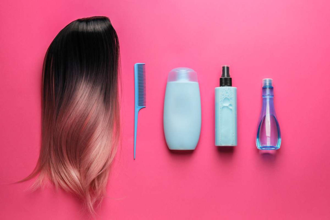 A wig, comb, and several wig care products on a hot pink background.