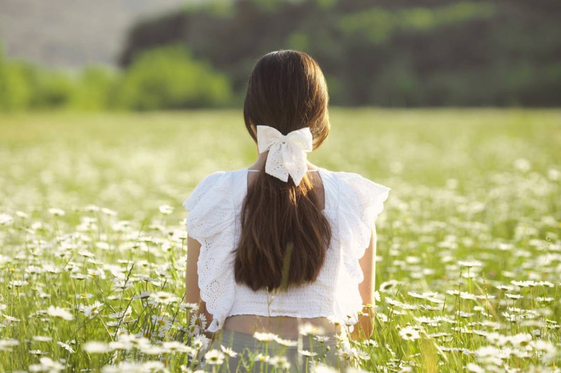 A woman in a field of daisies with a white bow in her long hair.