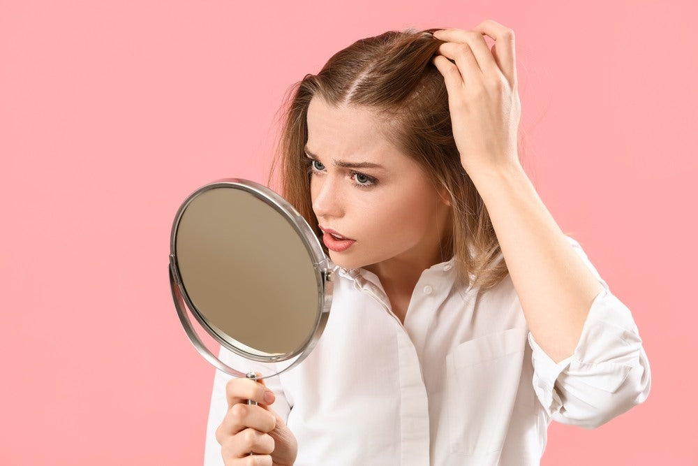 A young woman with hair loss inspects her scalp with concern