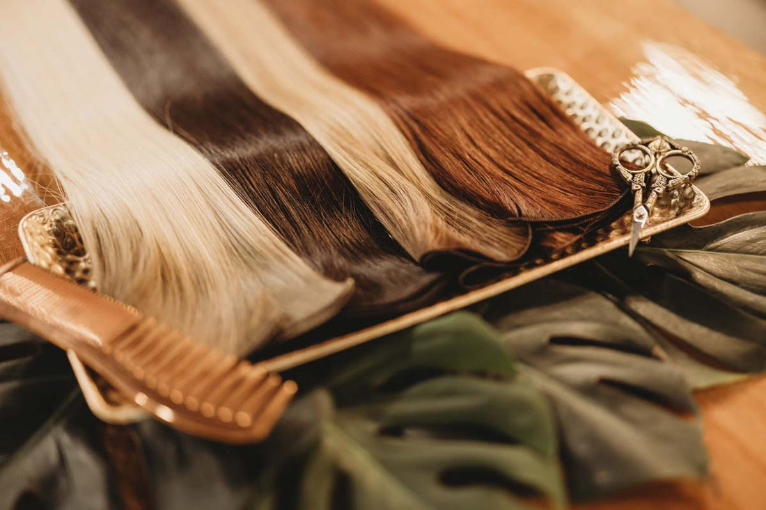 Multiple colors of hair extensions, a comb, and scissors on a silver tray.