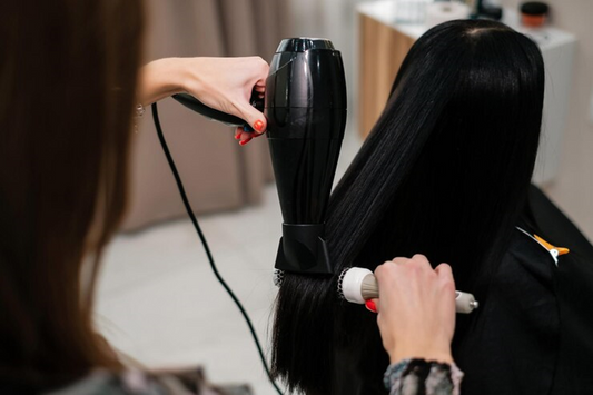 Person using a blow dryer and round brush to style long, straight hair, focusing on a smooth finish.