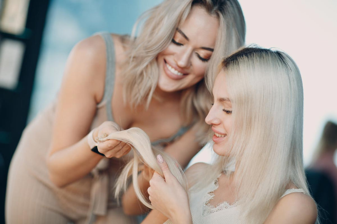Two blonde women inspect the quality of a hair extension.