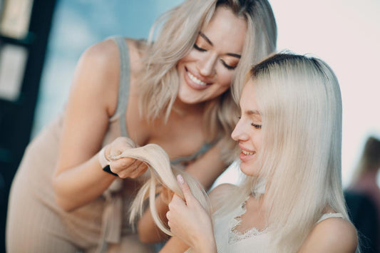 Two blonde women inspect the quality of a hair extension.