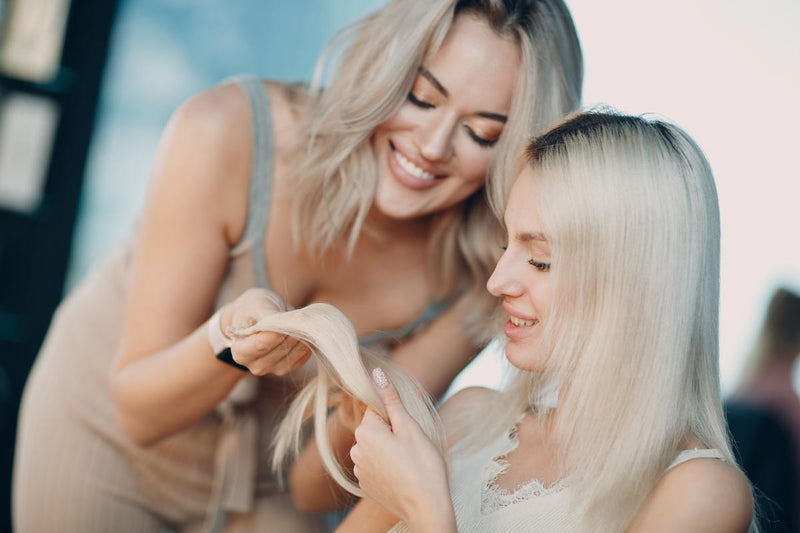 Two blonde women inspect the quality of a hair extension.