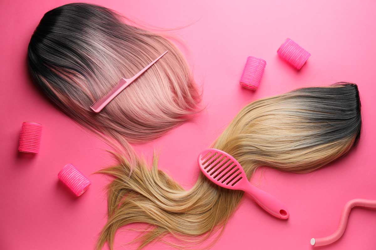 Two wigs on a pink background with brushes, combs, and curlers.