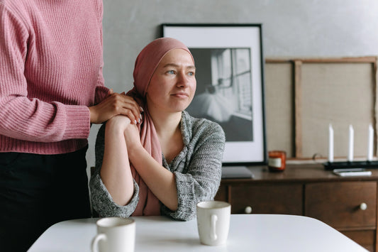 A woman suffering hair loss wearing a headscarf with another woman holding her hands.