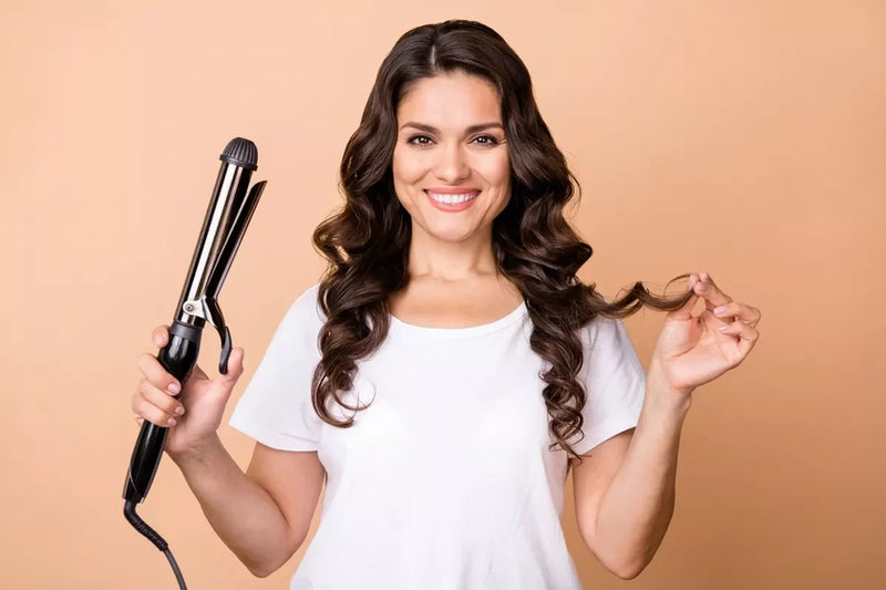 A smiling woman poses with a curling iron.