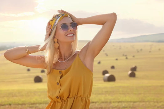 A smiling blonde in boho-style clothing in a field.