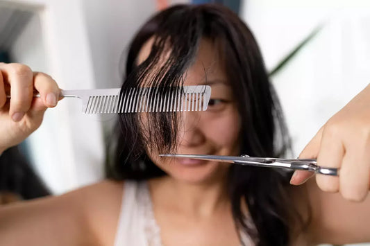 A smiling young woman cuts her own bangs.
