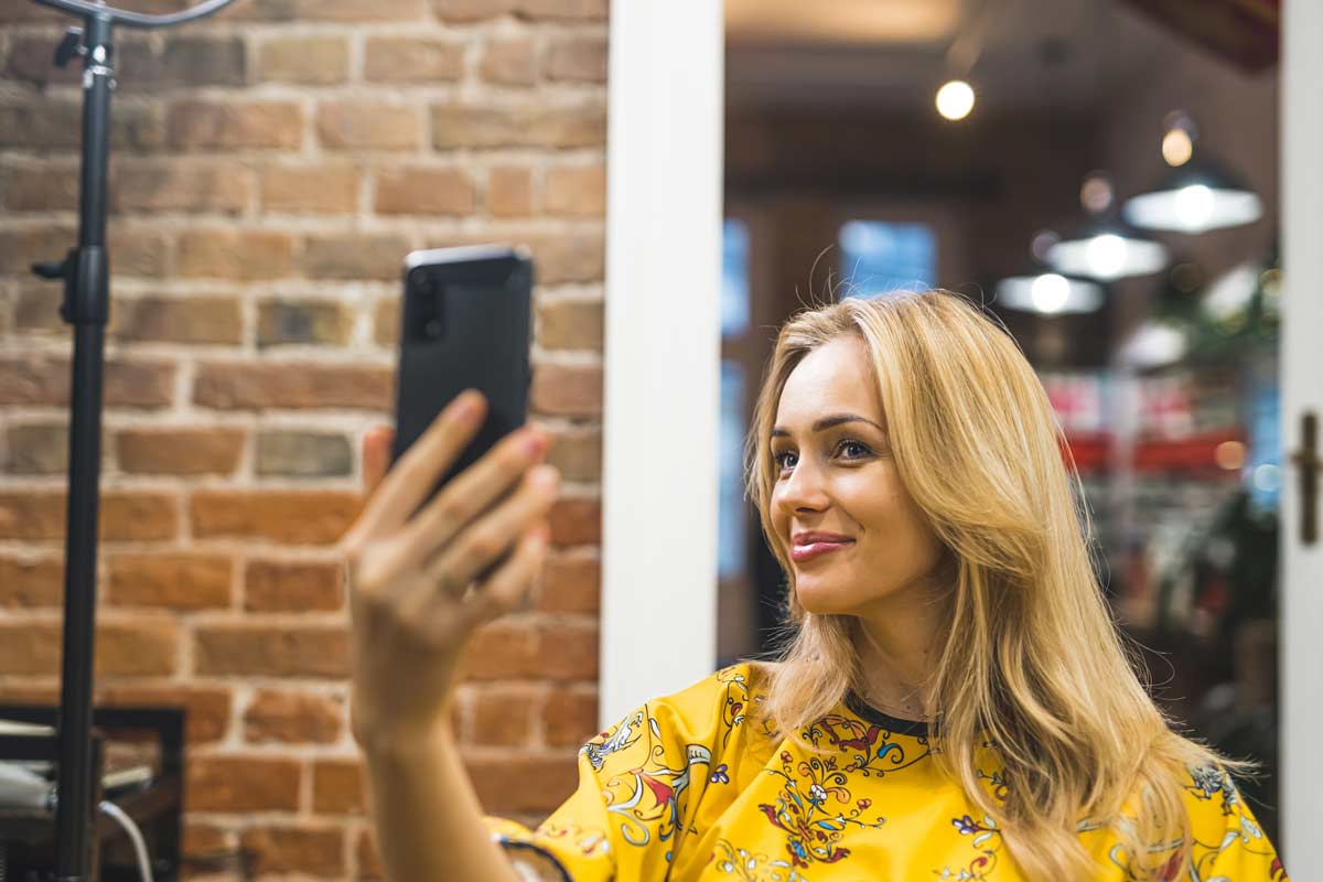 A happy,  young blonde woman takes a selfie after receiving a new hair topper