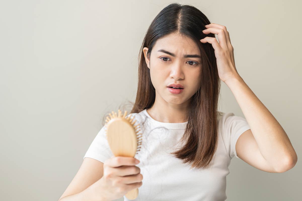 A young dark-haired woman with thinning hair looks anxiously at her hairbrush