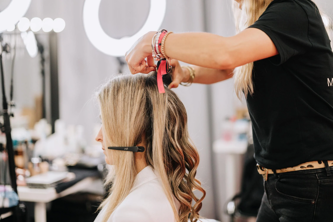 A stylist adding hair extensions to a blonde woman’s hair.