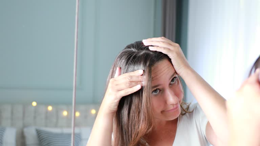 Woman examining her scalp in the mirror, parting her hair with her hands to check for hair thinning.