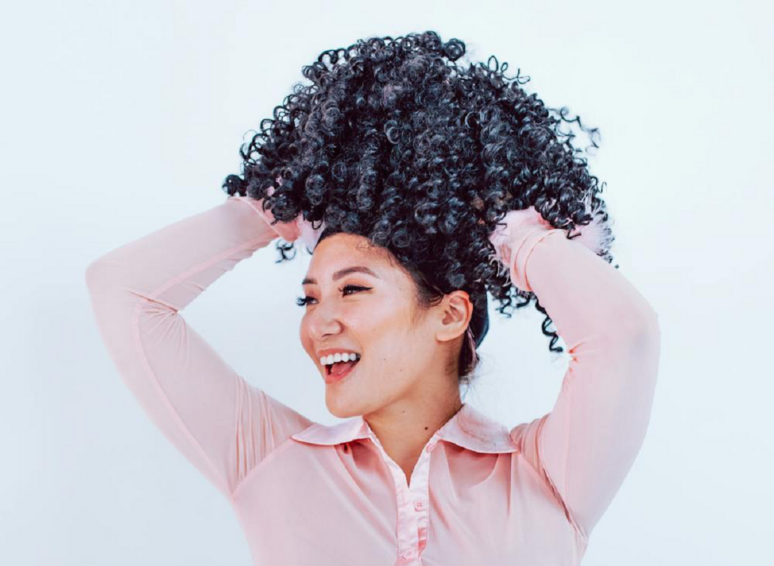 Image of a girl holding a curly wig above her head.