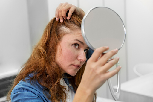 Image of lady with red hair checking her scalp for hair regrowth in the mirror. Taken from FreePik
