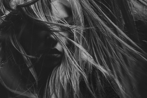 A grayscale image of a woman with blonde hair blowing in front of her face.