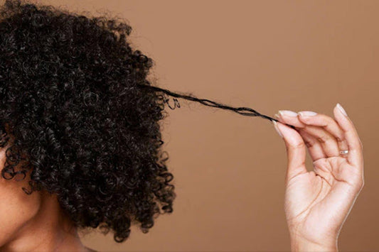 A woman with short, tight curly hair holding one of her strands out