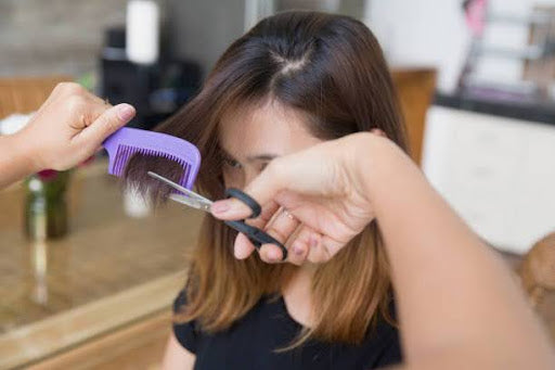 Woman with shoulder length hair getting her bangs trimmed.