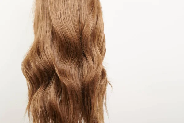 A close-up of long, wavy, light brown balayage hair against a plain white background, showcasing a soft and smooth texture.