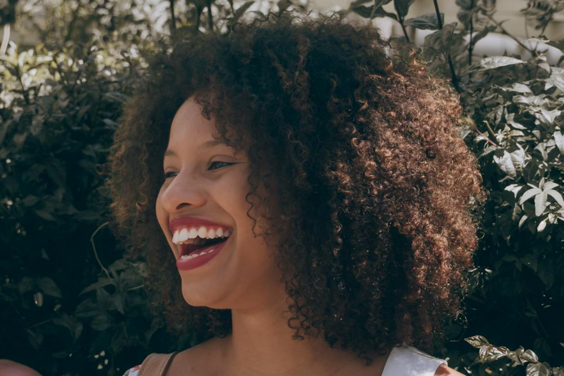 Image of a woman smiling with medium length curly hair. Taken from Pexels