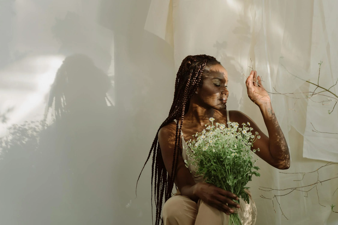 An artsy shot of a woman with ultra-long knotless braids holding flowers.