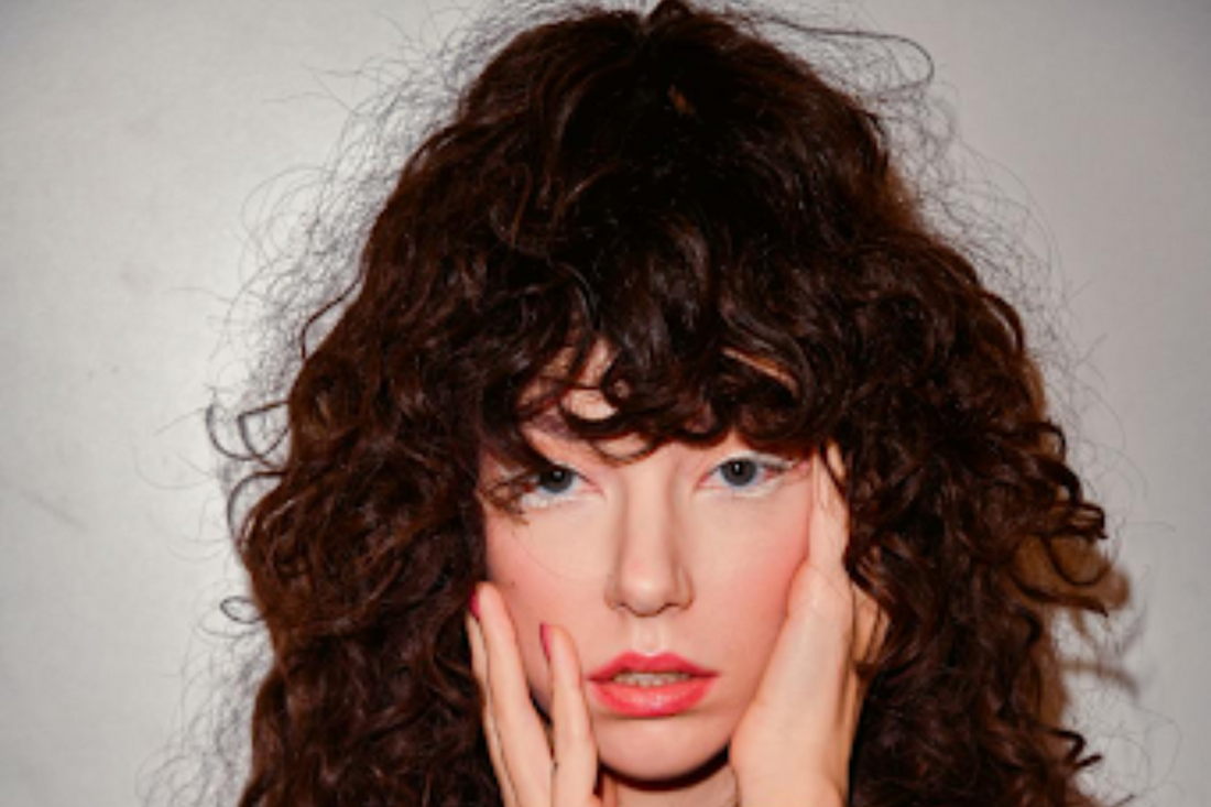 A close-up of a brunette model with long curly hair with bangs.