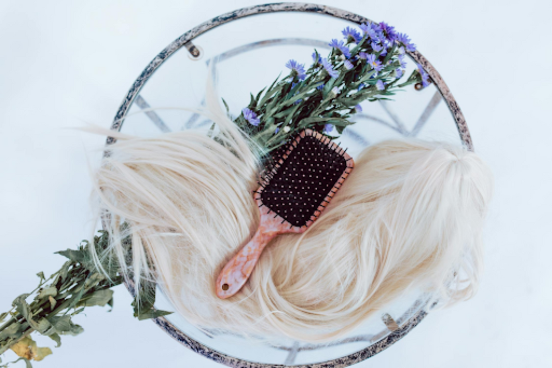 Light blonde hair extensions placed on a table with flowers and a hair brush.