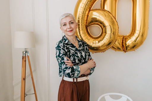 A woman with short, fine hair crossing her arms in front of ‘60’ balloons.