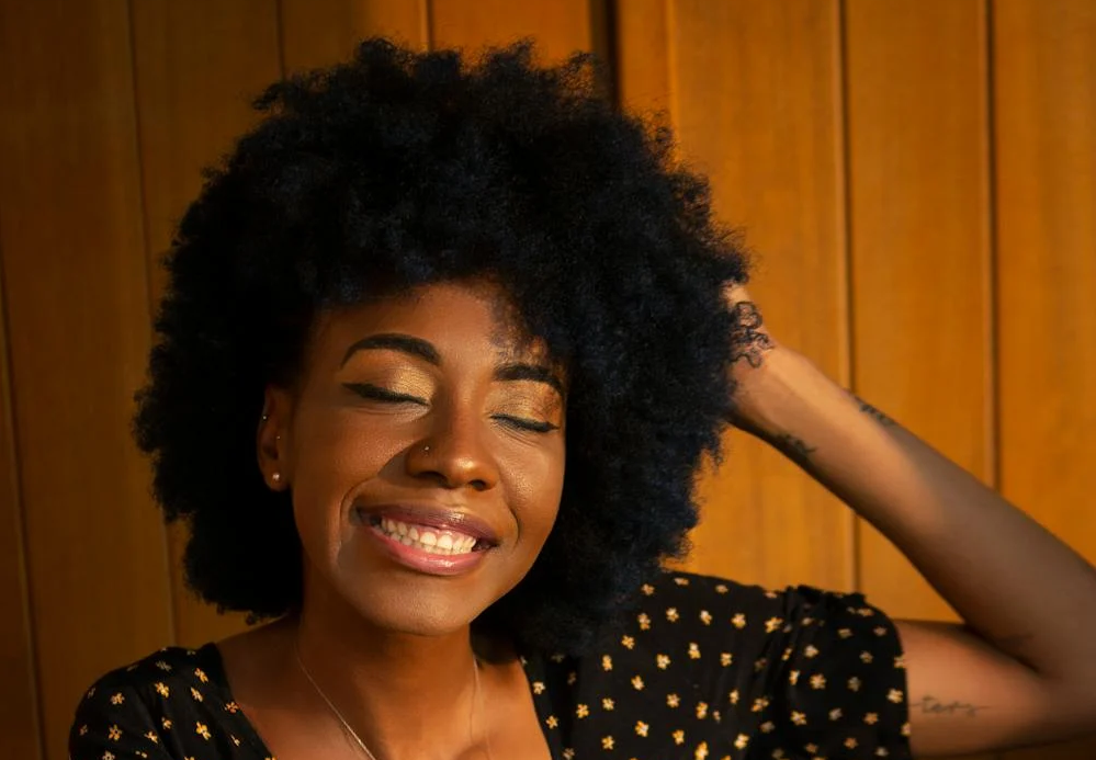 A black woman with natural, curly hair smiling into the camera.