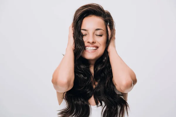 Smiling woman with long, thick dark hair, eyes closed, and hands gently holding her hair against a plain white background.