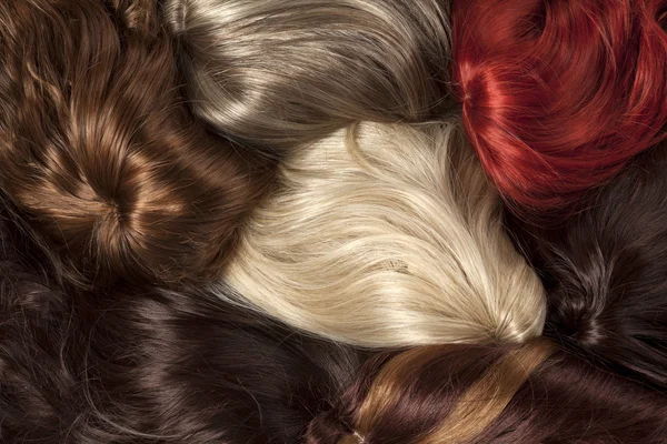 A close-up arrangement of various hair swatches in different colors, including blonde, red, brown, and black, showcasing smooth and shiny textures.