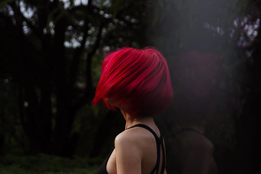 A woman swaying her bright red hair in a dark forest.