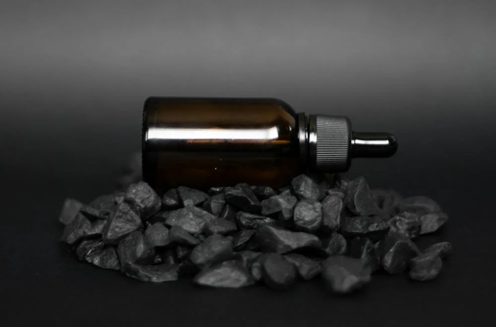 A black castor oil bottle with dropper positioned on black rocks.