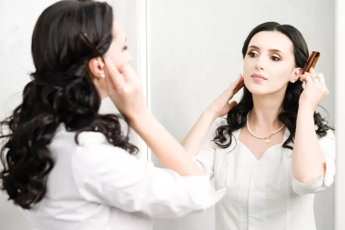 A curly haired woman styles her hair in a vanity mirror.