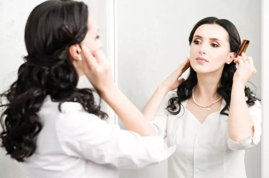 A curly haired woman styles her hair in a vanity mirror.